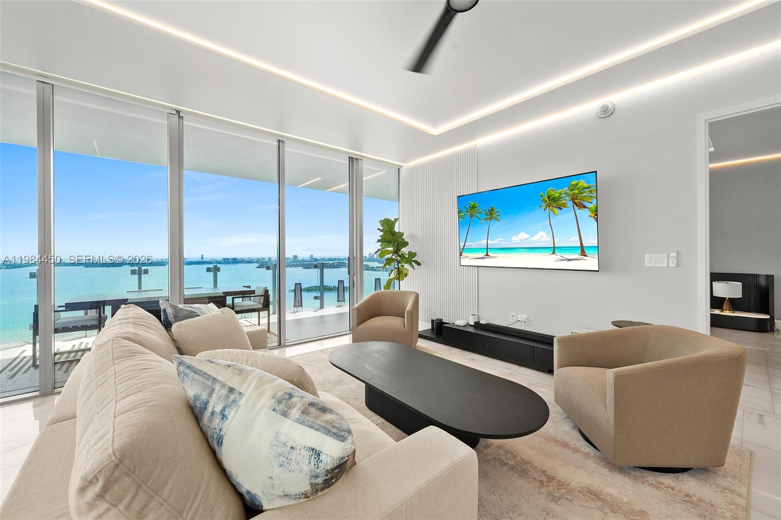 A modern living room features a beige sofa, two armchairs, and a wall-mounted television — 700 NE 26th Ter # 3401, Miami FL 33137, MIAMI, FL
