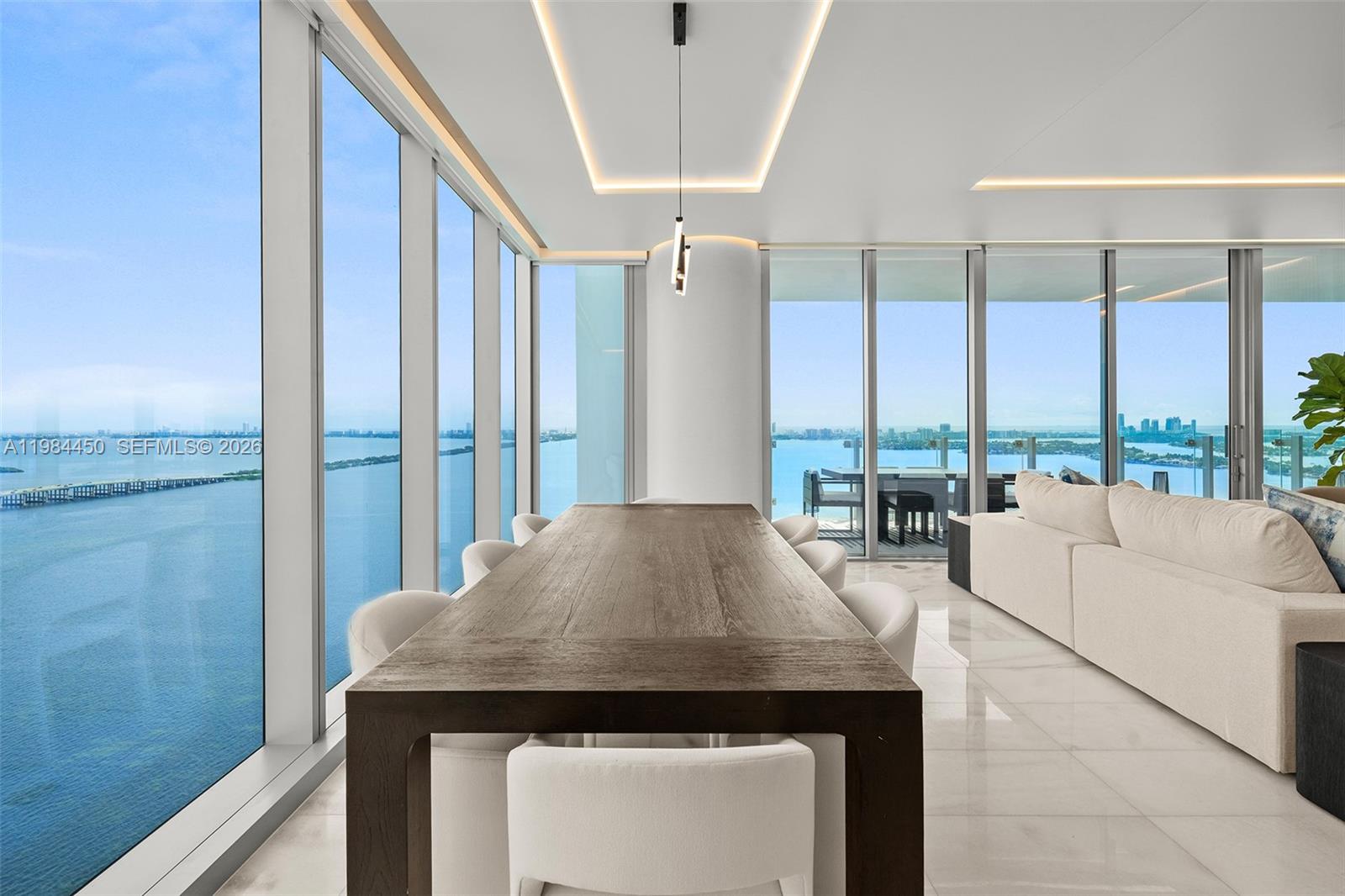 A dining room with a dark wooden table, white chairs, and floor-to-ceiling water views — 700 NE 26th Ter # 3401, Miami FL 33137, MIAMI, FL