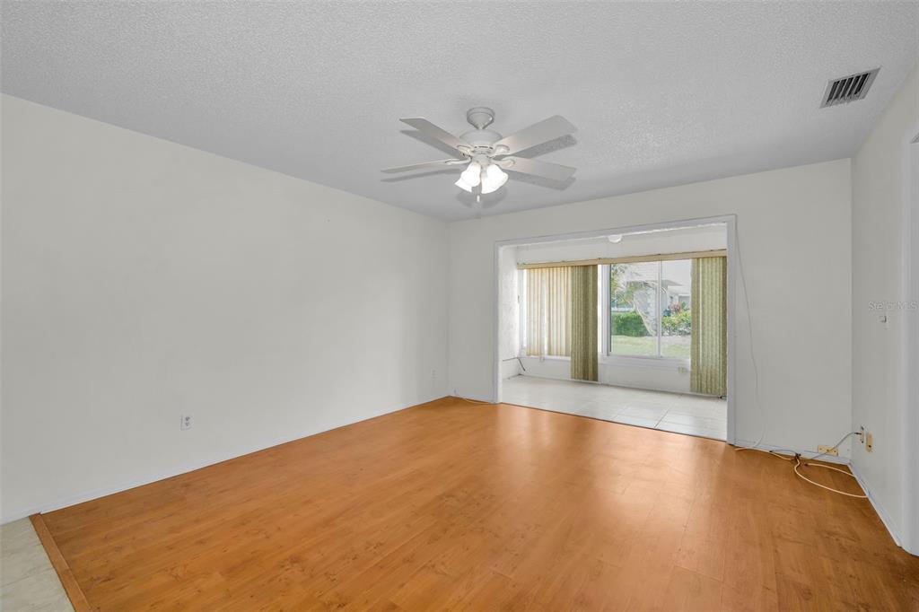 An empty room with wood-look flooring, a ceiling fan, and a view into a sunroom — 3819 TEESIDE DRIVE, NEW PORT RICHEY, FL