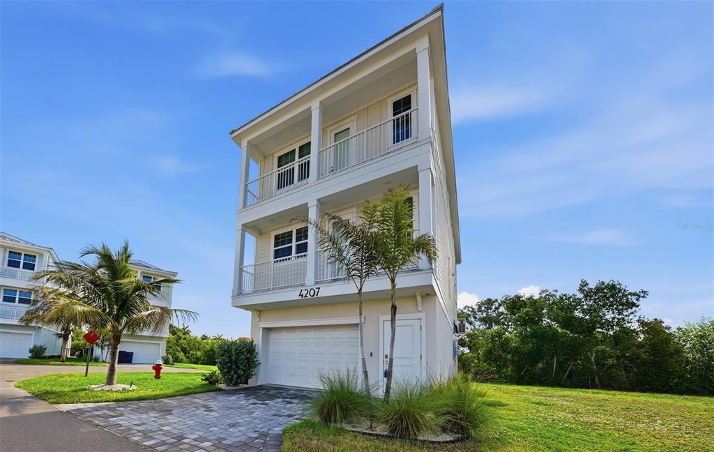 A three-story coastal house with a garage, balconies, and palm trees under a blue sky — 4207 MARINA VIEW WAY, CORTEZ, FL