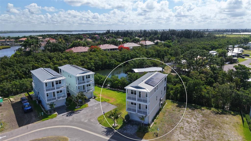 An aerial view shows three multi-story houses with metal roofs and solar panels near water — 4207 MARINA VIEW WAY, CORTEZ, FL