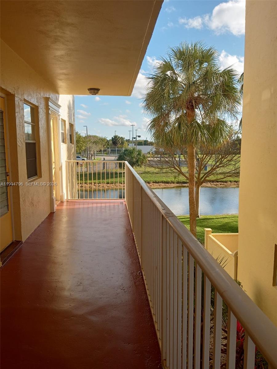 A covered balcony with a red floor overlooks a pond and a palm tree — LAUDERDALE LAKES, FL