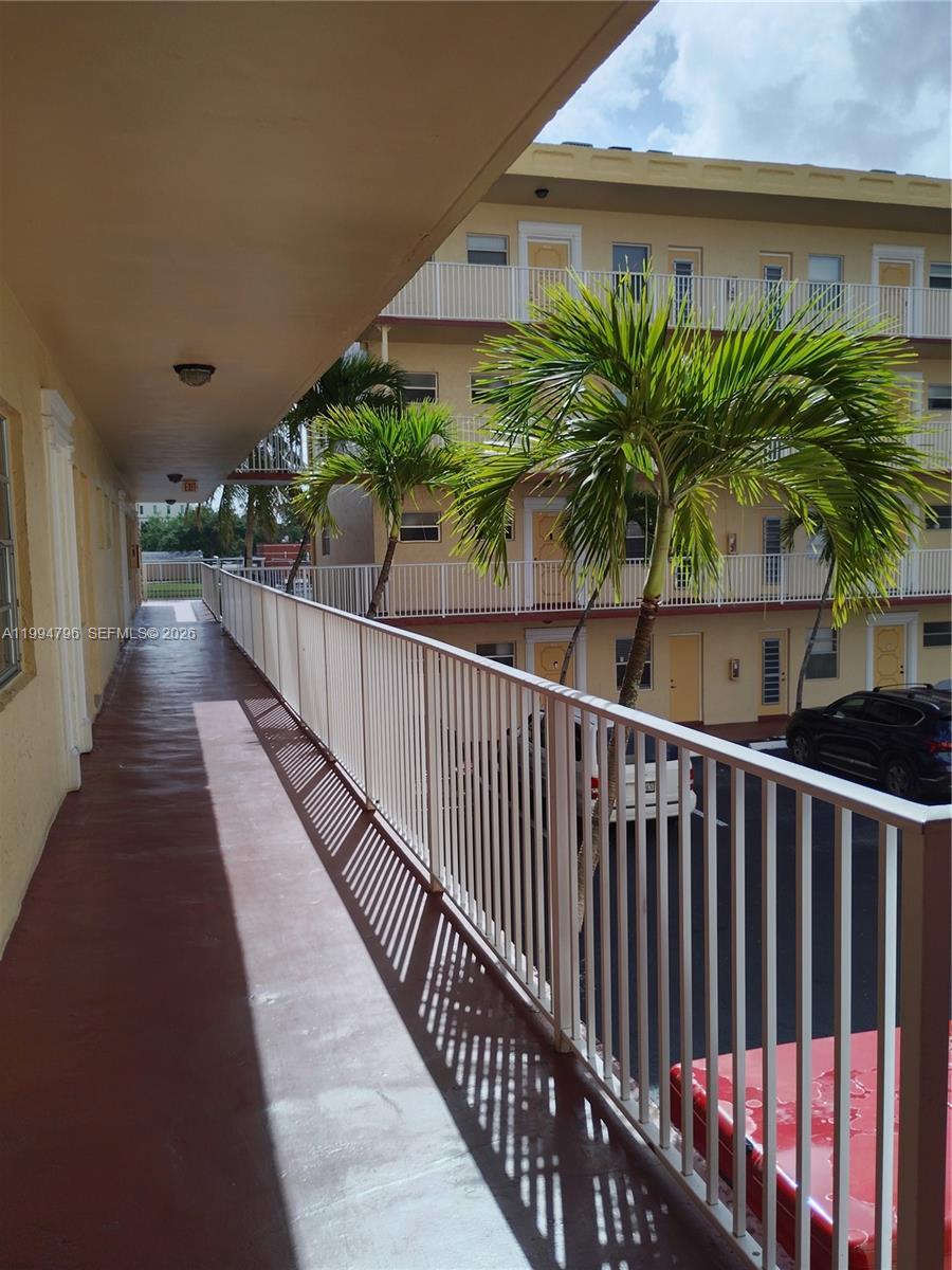 An exterior walkway with a white metal railing overlooks a courtyard with palm trees — LAUDERDALE LAKES, FL