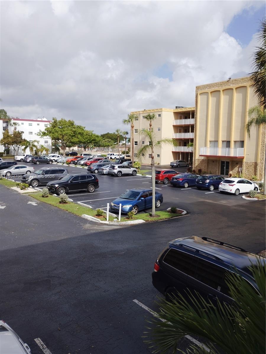 An outdoor parking lot with multiple cars sits in front of a multi-story apartment building — LAUDERDALE LAKES, FL