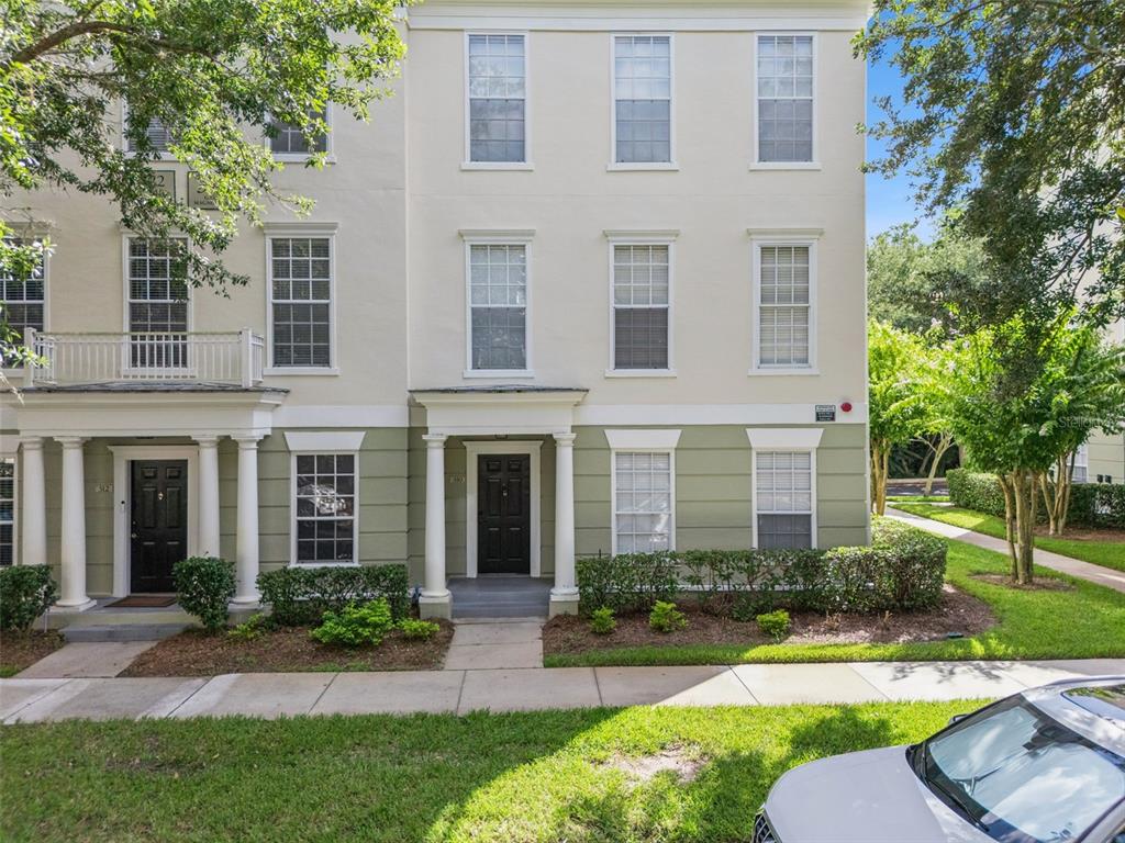 A three-story townhouse exterior features a black front door, white columns, and green siding — 310 GRAND MAGNOLIA AVENUE UNIT 310, CELEBRATION, FL