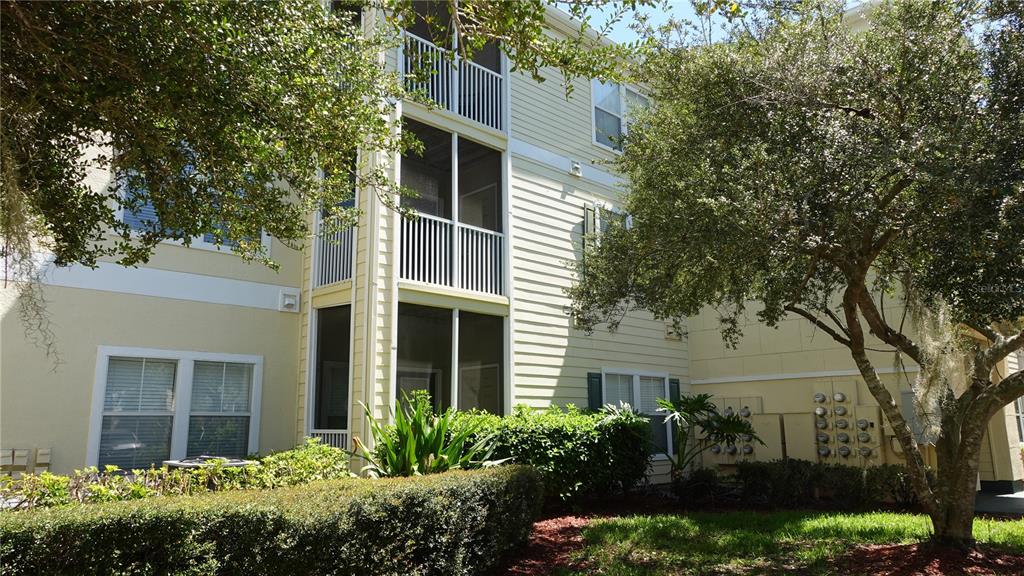 A three-story apartment building features light yellow siding, screened balconies, and surrounding landscaping — 18281 BRIDLE CLUB DRIVE, TAMPA, FL