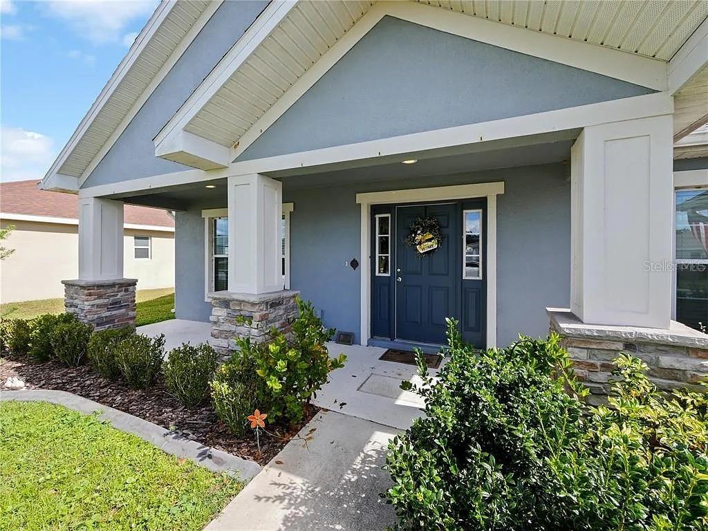 A blue house exterior features a covered front porch with stone-based columns and a door — 218 CATTAIL WAY, LAKE ALFRED, FL