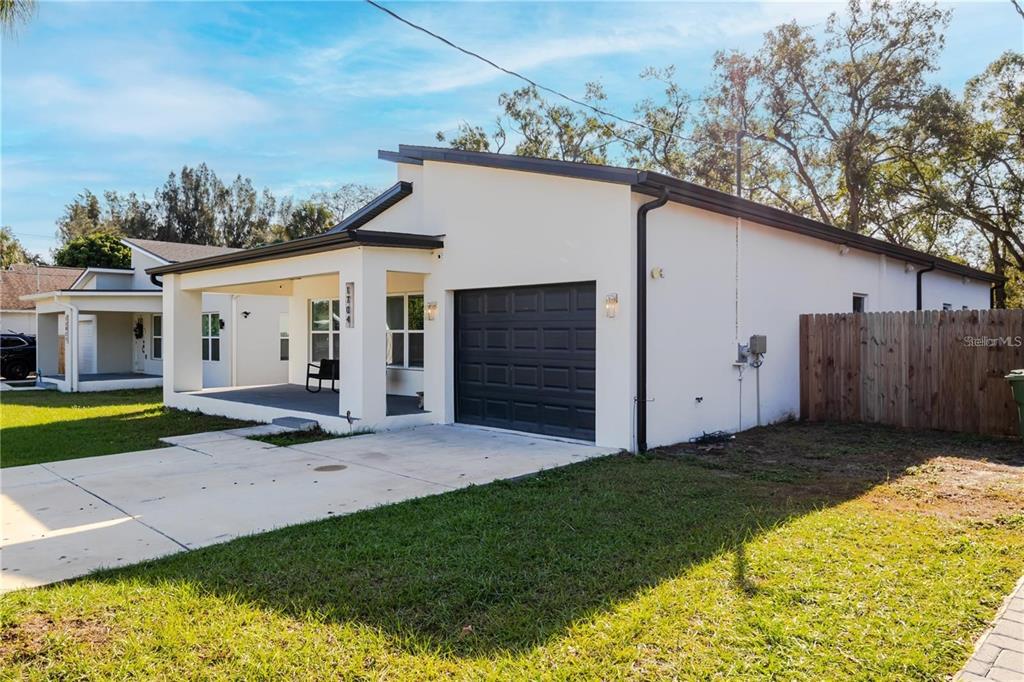 A white single-story house with a dark garage door and a covered front porch — 1704 W HANNA AVENUE, TAMPA, FL