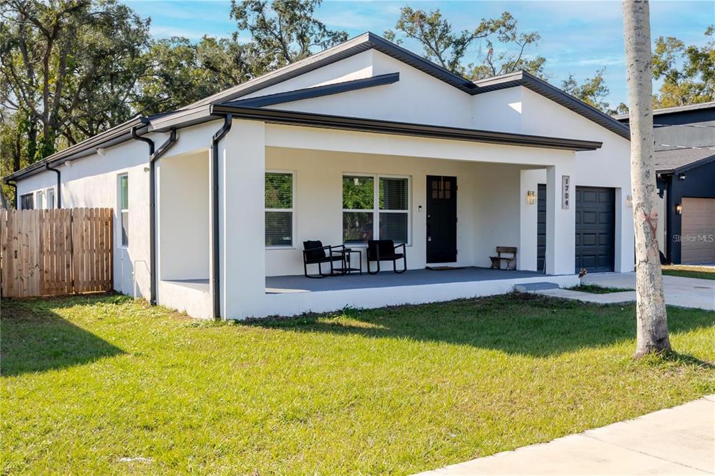 A white single-story house features a covered front porch, black trim, and a garage — 1704 W HANNA AVENUE, TAMPA, FL