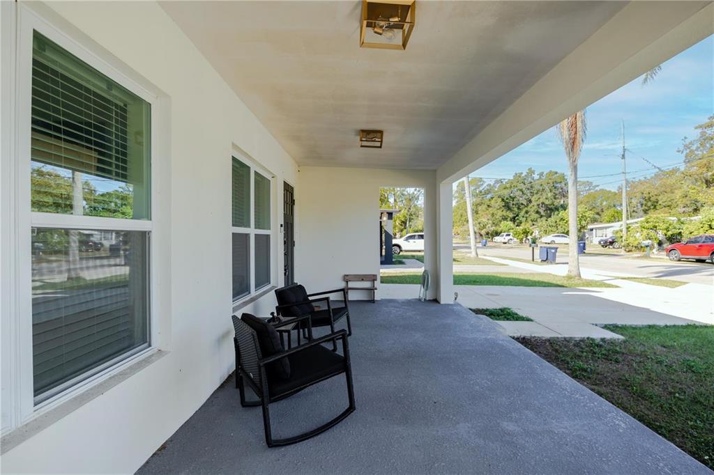 A covered front porch features a concrete floor, two black chairs, and white exterior walls — 1704 W HANNA AVENUE, TAMPA, FL