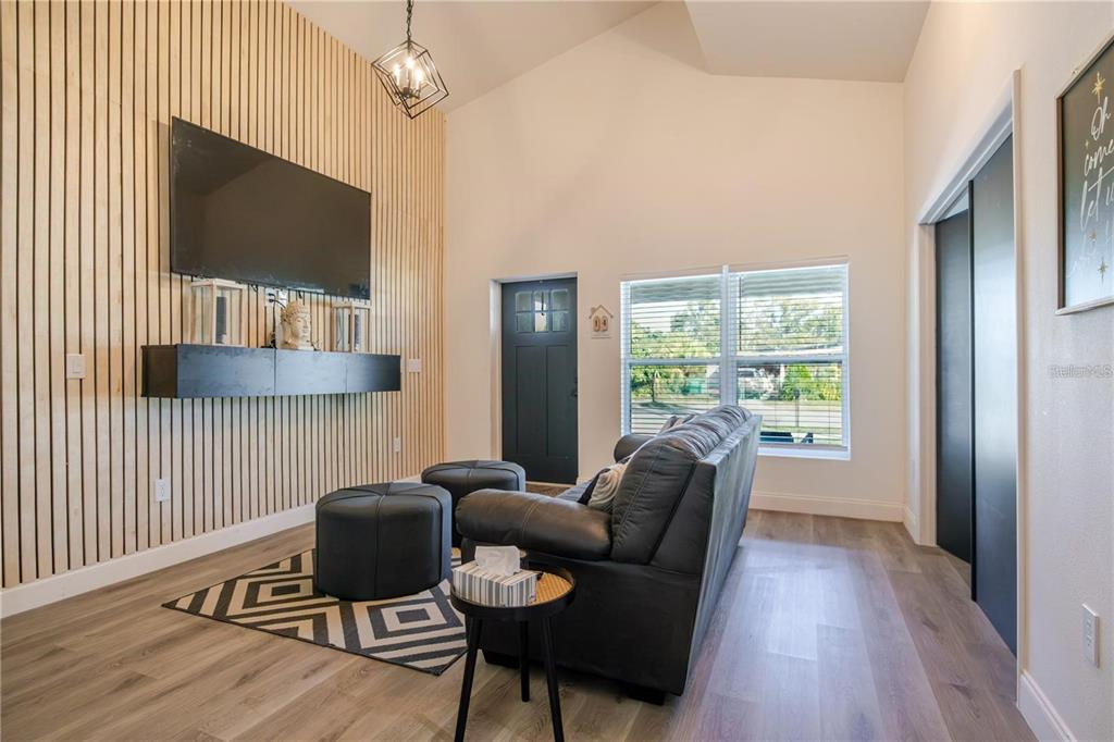 A living room features a wood-slat accent wall, a mounted television, and a dark sofa — 1704 W HANNA AVENUE, TAMPA, FL