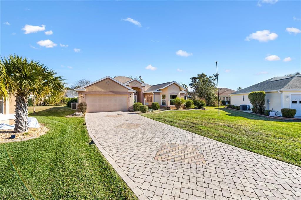 A single-story house with a paved driveway and a two-car garage under a blue sky — 1505 DORIA LANE, LADY LAKE, FL