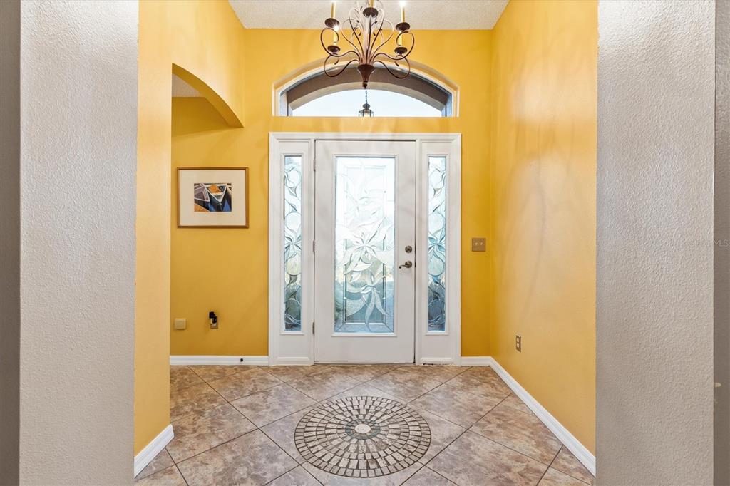 A foyer with yellow walls, tile flooring, a decorative medallion, and a glass-paneled front door — 1505 DORIA LANE, LADY LAKE, FL