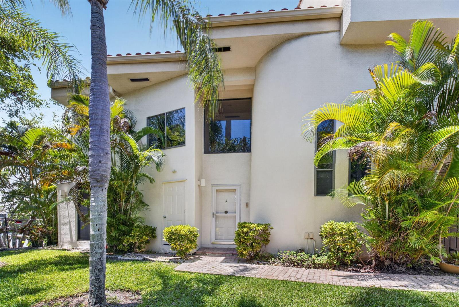 A two-story stucco building with a brick walkway, palm trees, and a white front door — 1111 George Bush Boulevard # A, Delray Beach FL 33483, DELRAY BEACH, FL