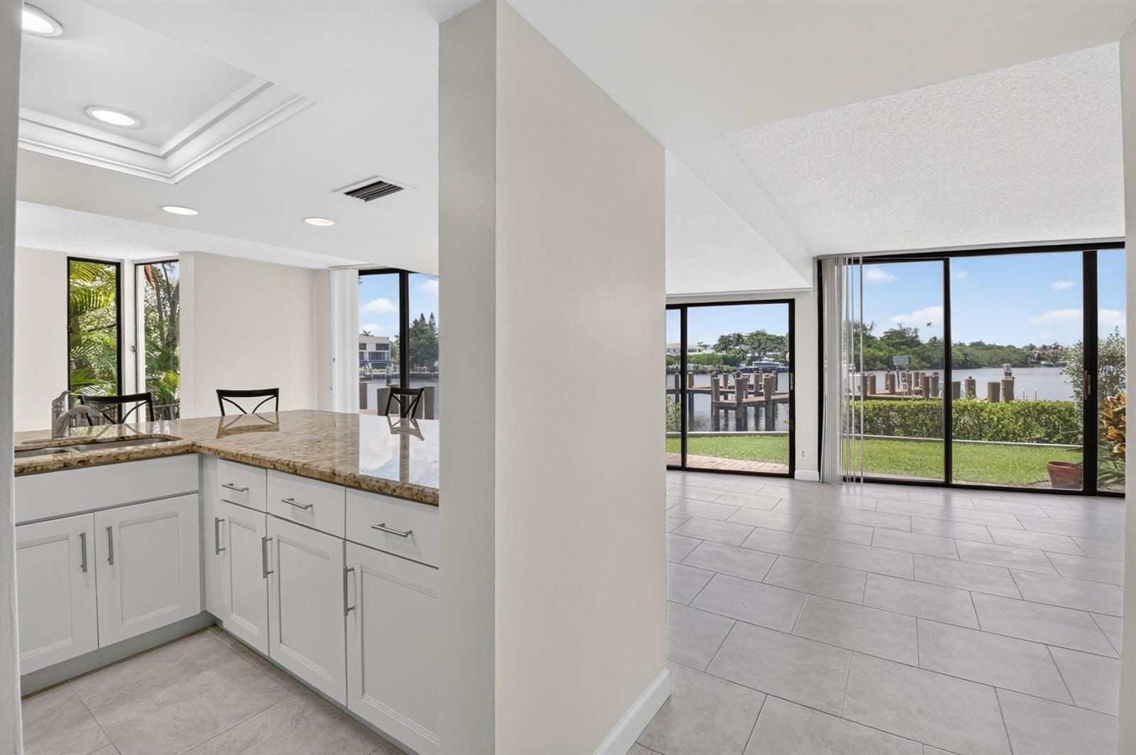 A kitchen with granite countertops and white cabinets overlooks a living area with water views — 1111 George Bush Boulevard # A, Delray Beach FL 33483, DELRAY BEACH, FL