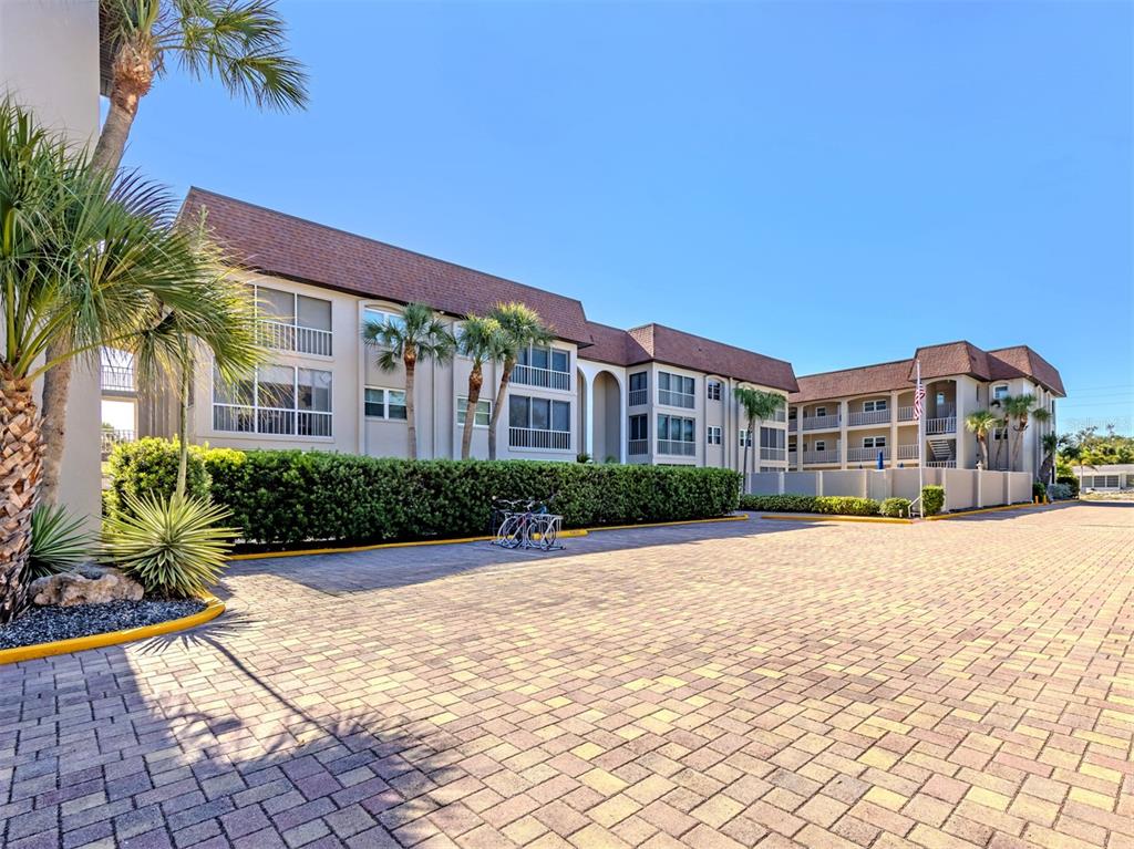 A multi-story apartment building with a paved courtyard and palm trees under a clear sky — 101 PARK BOULEVARD S UNIT 106, VENICE, FL