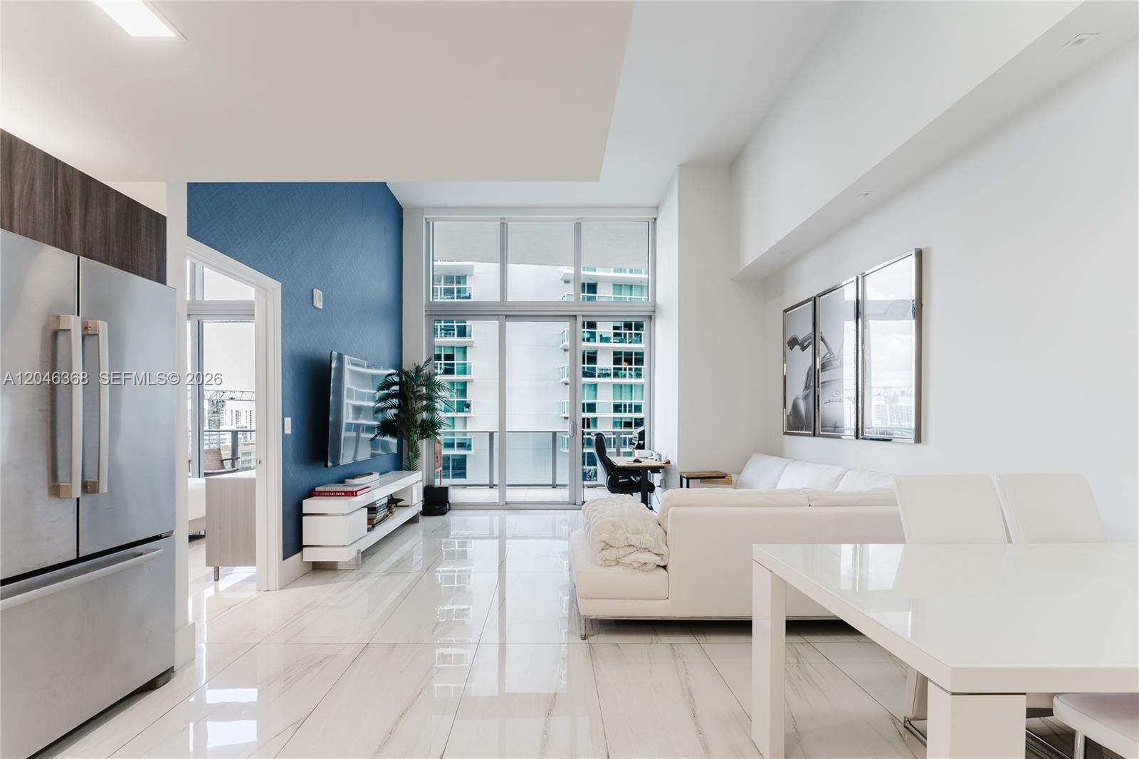 A modern living room features white tile floors, a blue accent wall, and floor-to-ceiling windows — 488 NE 18th St # 1205, Miami FL 33132, MIAMI, FL