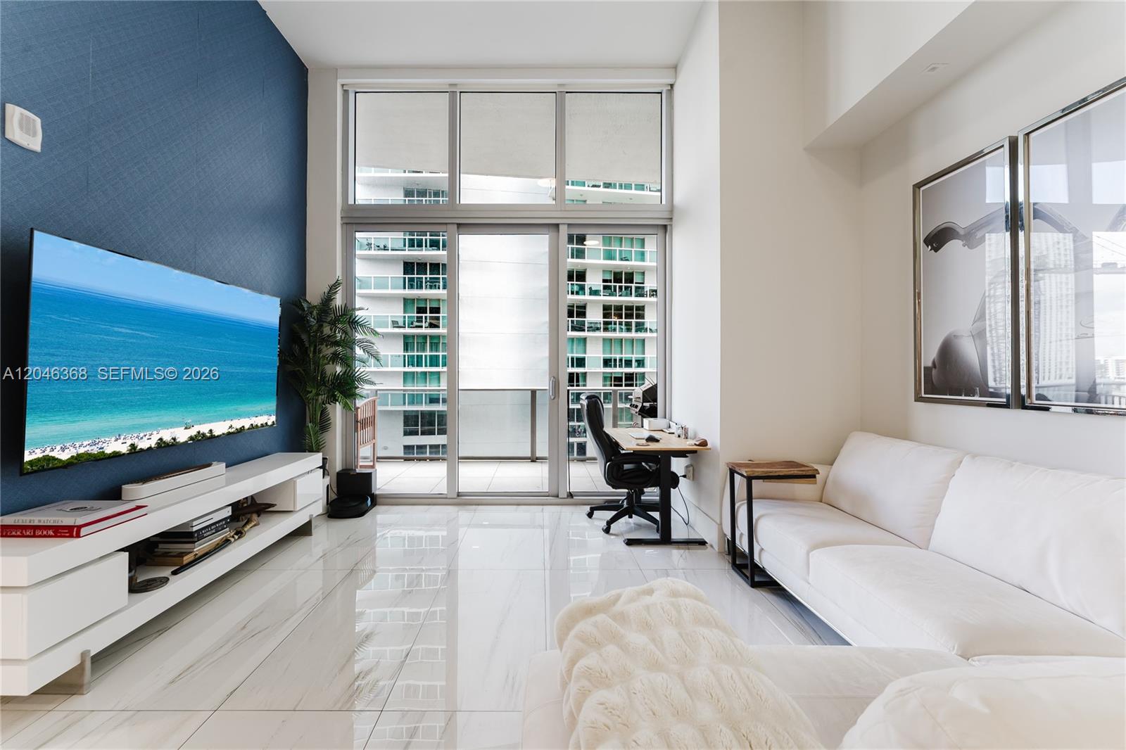 A modern living room features a blue accent wall, white sofa, and floor-to-ceiling windows — 488 NE 18th St # 1205, Miami FL 33132, MIAMI, FL