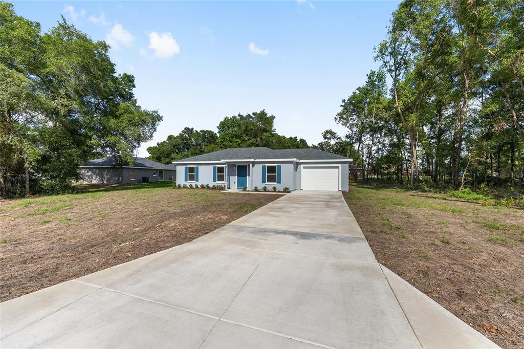 A single-story gray house with a concrete driveway and blue shutters sits on a lot — 37 DOGWOOD DRIVE PASS, OCALA, FL