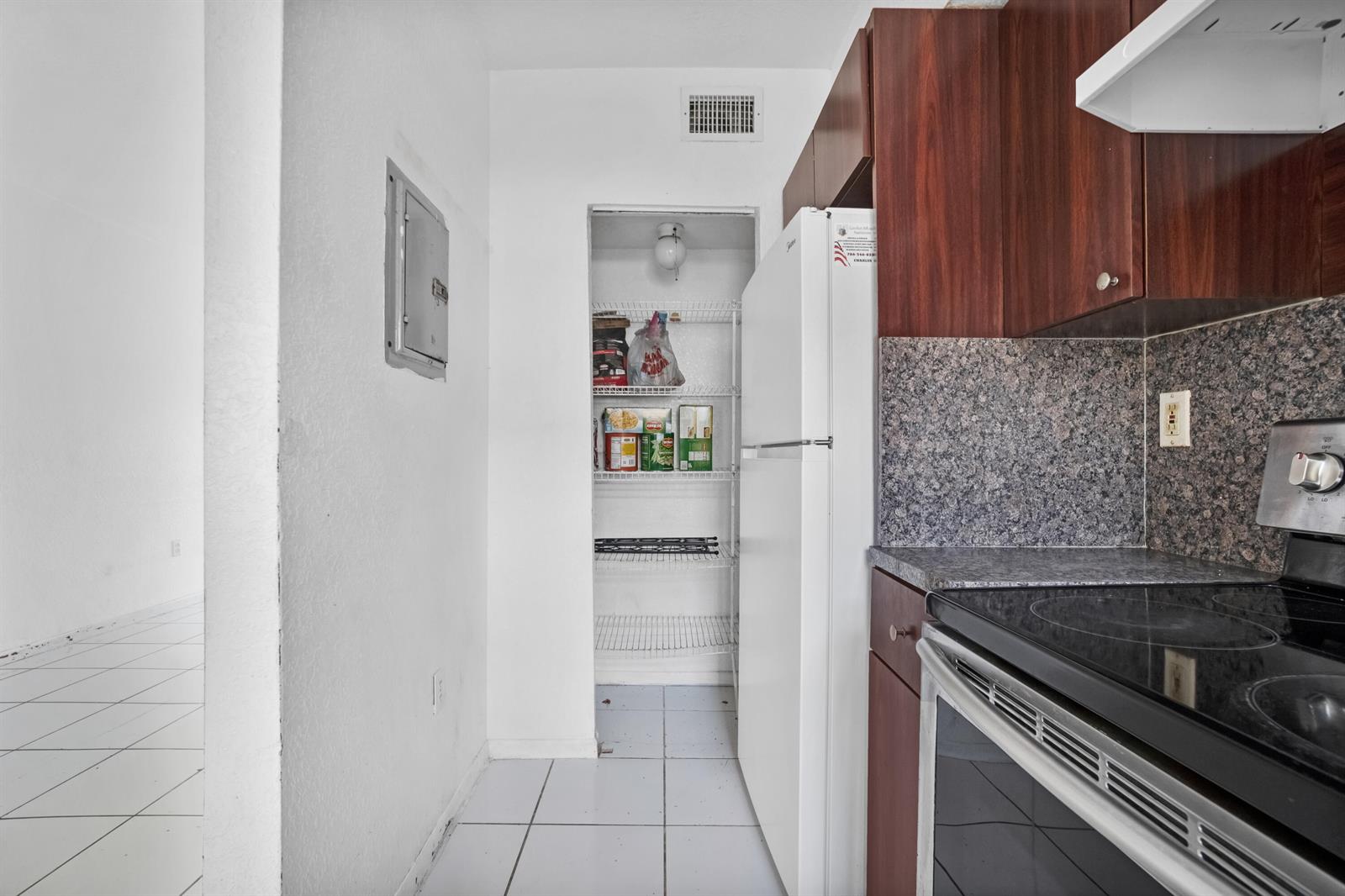 A kitchen features dark wood cabinets, a white refrigerator, a pantry, and a tiled floor — 306 NW 84th Terrace # 306, Miami FL 33150, MIAMI, FL