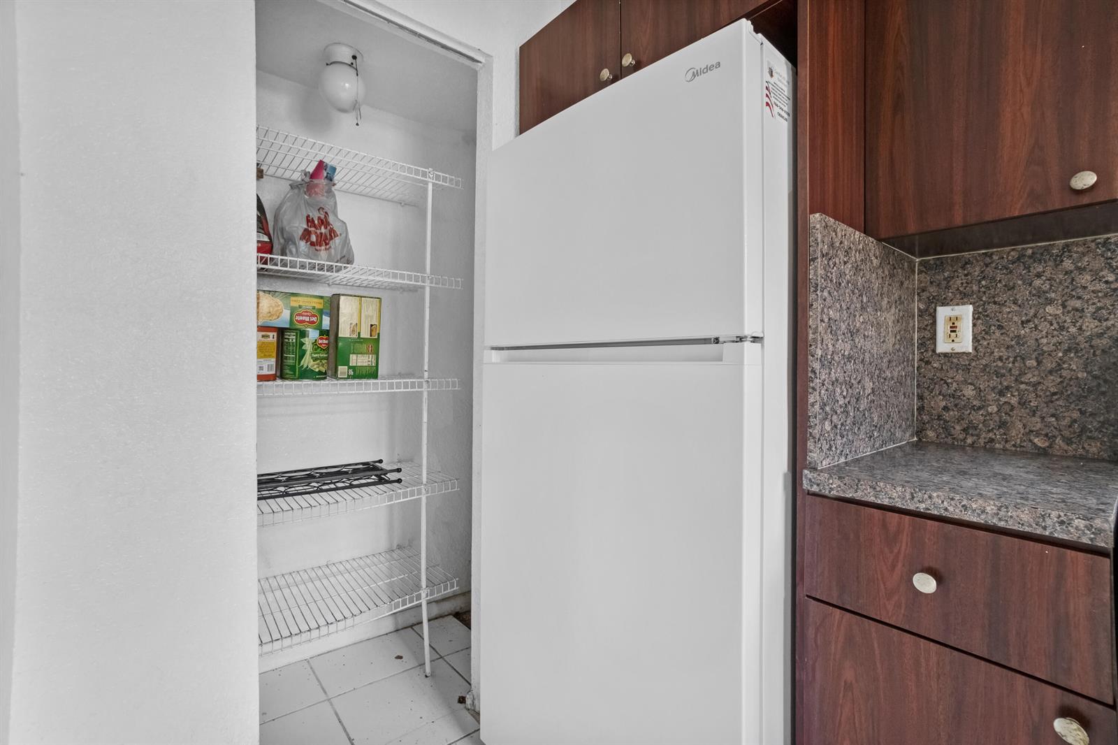 A white refrigerator stands next to a pantry with wire shelving in a kitchen — 306 NW 84th Terrace # 306, Miami FL 33150, MIAMI, FL