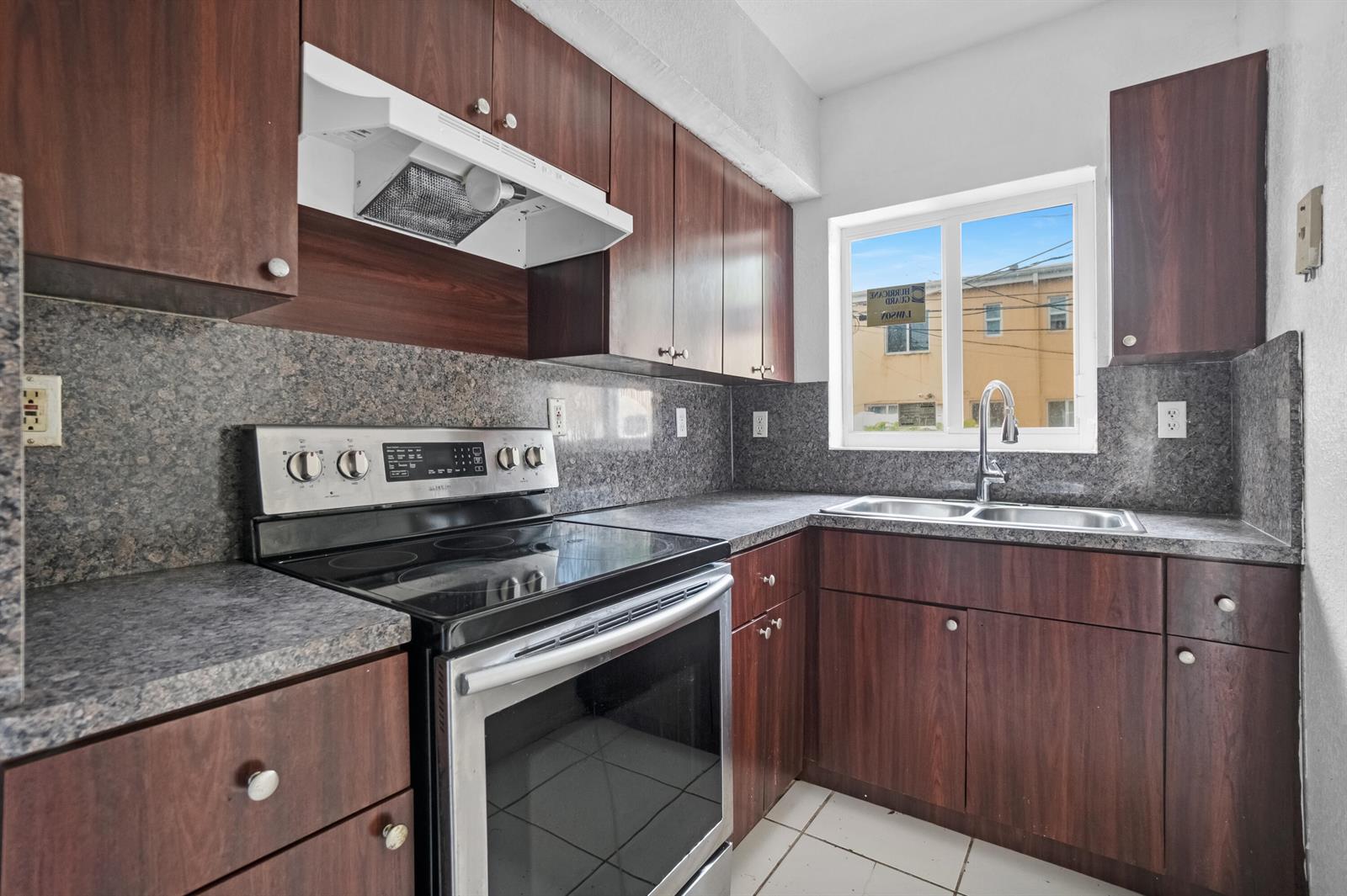 A kitchen features dark wood cabinets, granite countertops, a stainless steel stove, and a window — 306 NW 84th Terrace # 306, Miami FL 33150, MIAMI, FL