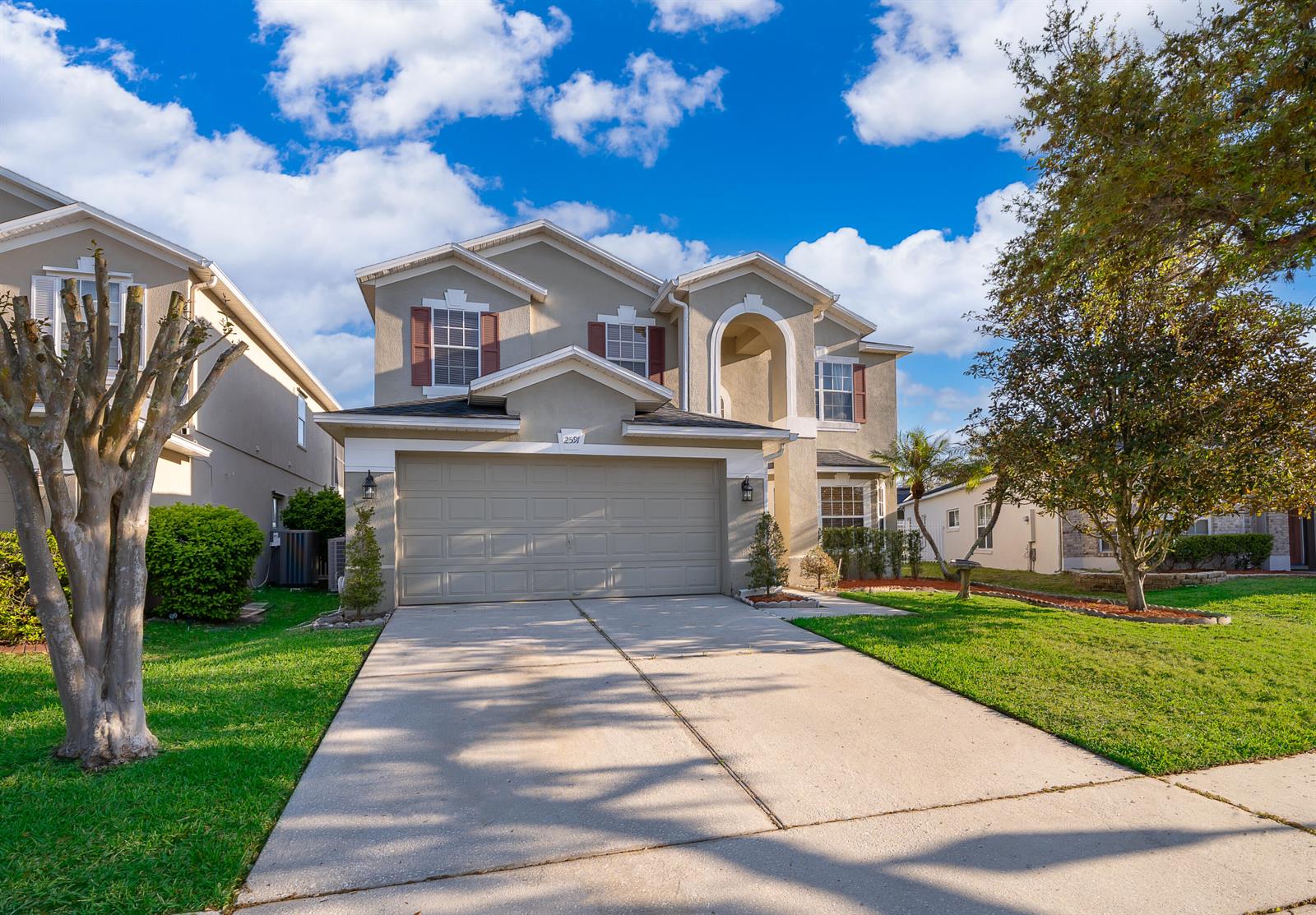 A two-story suburban house features a beige stucco exterior, a two-car garage, and a driveway — 2591 Dover Glen Circle, Orlando FL 32828, ORLANDO, FL