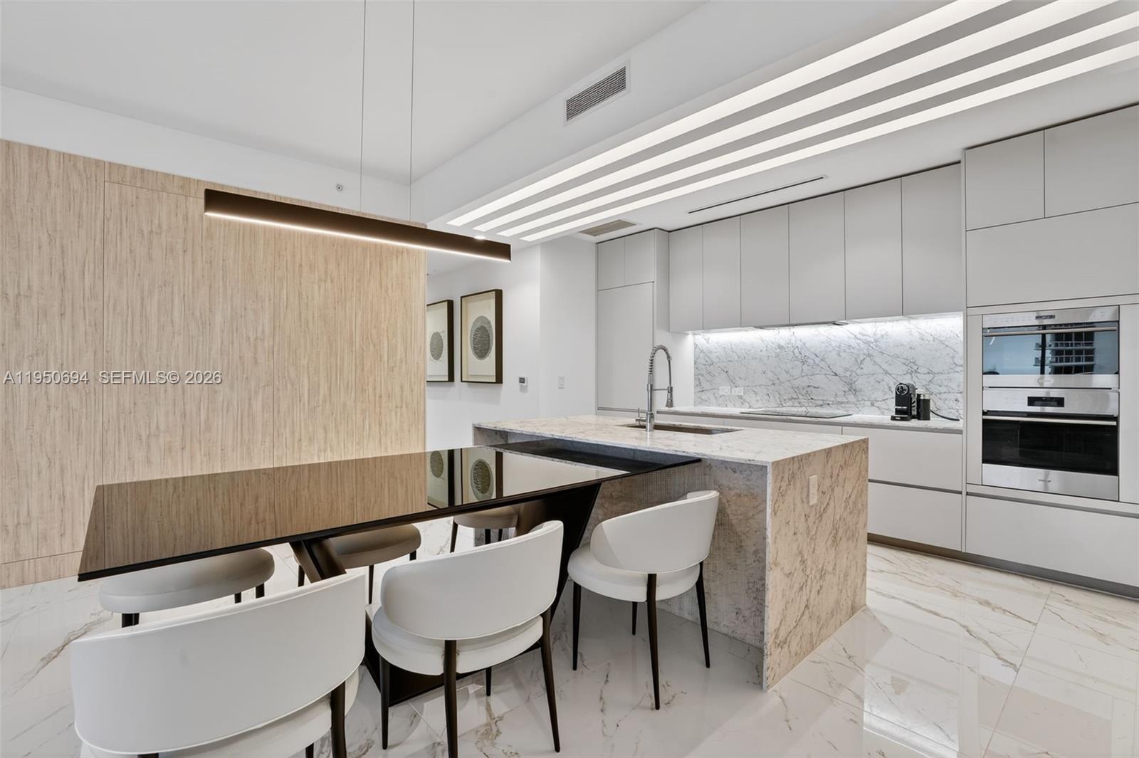 A modern kitchen features a marble island, integrated appliances, and an attached dining table — 5775 Collins Ave # 405, Miami Beach FL 33140, MIAMI BEACH, FL