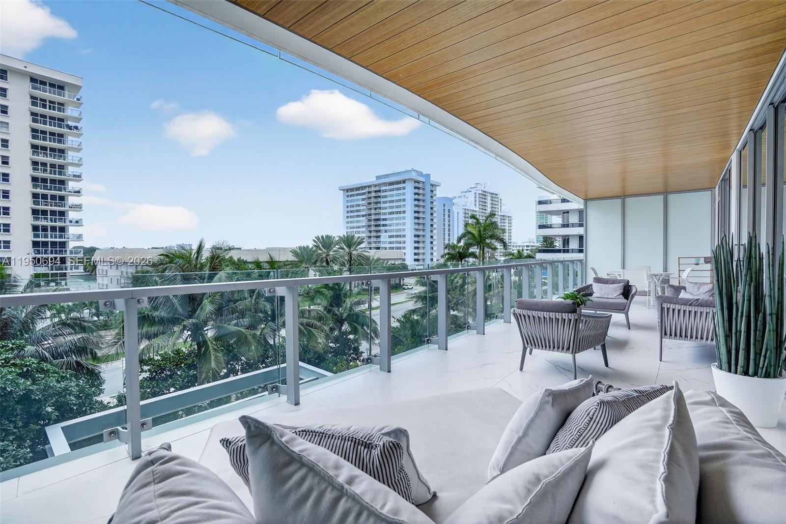 A spacious balcony features modern outdoor furniture, a glass railing, and views of surrounding buildings — 5775 Collins Ave # 405, Miami Beach FL 33140, MIAMI BEACH, FL