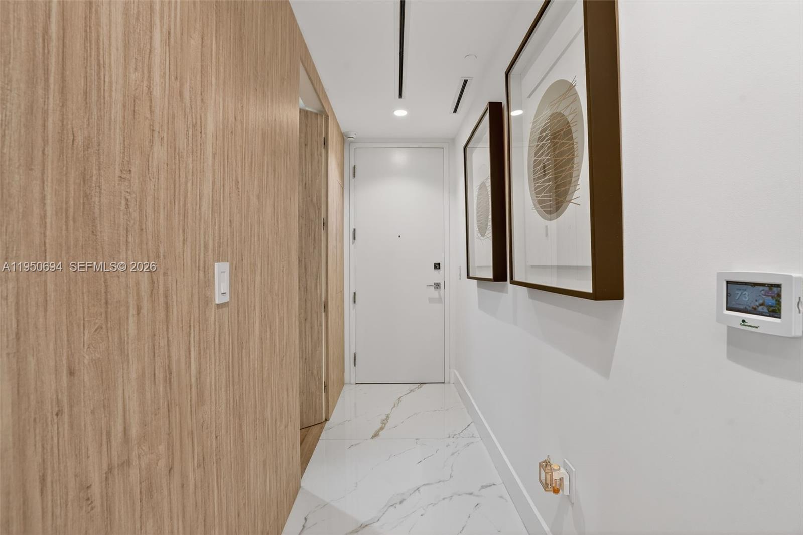 A hallway features wood-paneled walls, white marble flooring, two framed artworks, and a white door — 5775 Collins Ave # 405, Miami Beach FL 33140, MIAMI BEACH, FL