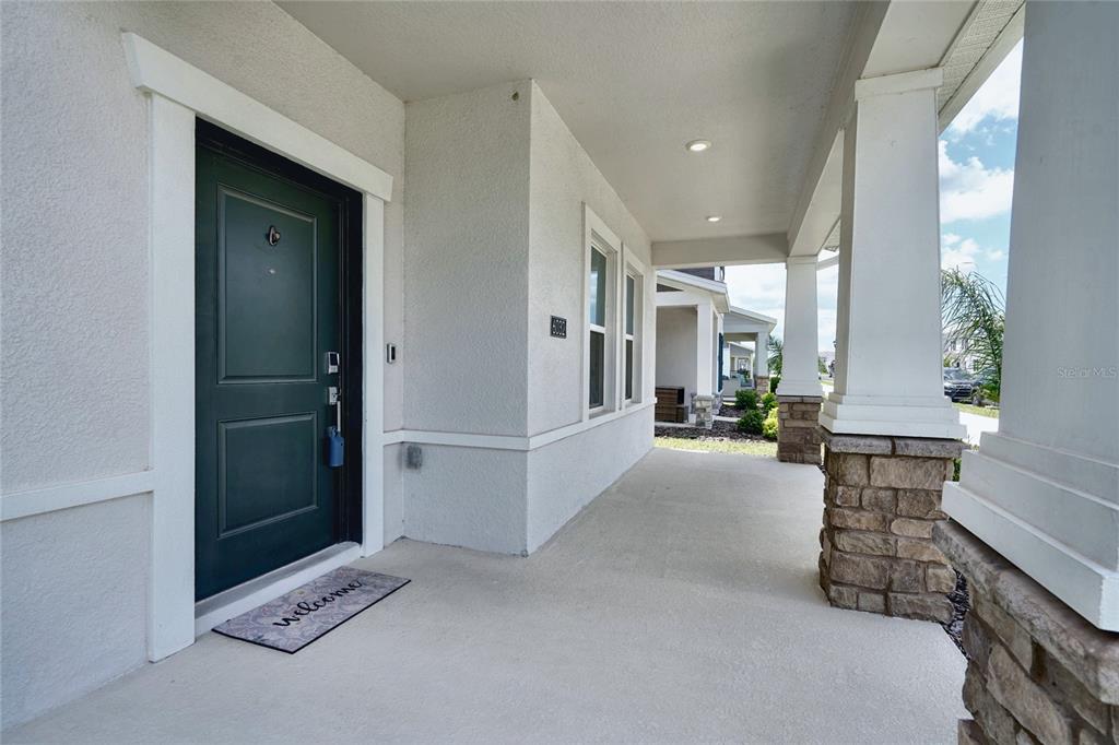 A covered front porch features a dark green door, stone-based columns, and a welcome mat — 6032 BLISSFUL STREET, CLERMONT, FL