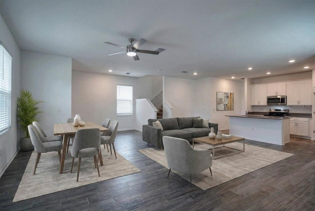 An open-concept living and dining area features gray wood-look flooring, neutral furniture, and white cabinetry — 6032 BLISSFUL STREET, CLERMONT, FL
