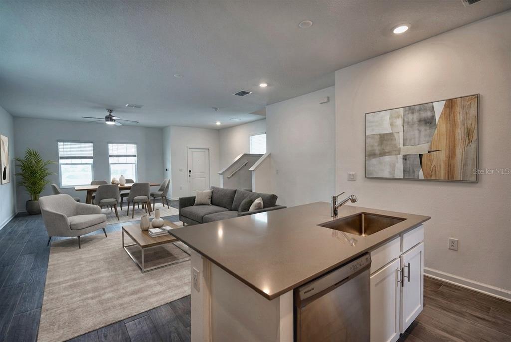 A kitchen island with a sink overlooks an open-concept living and dining area — 6032 BLISSFUL STREET, CLERMONT, FL