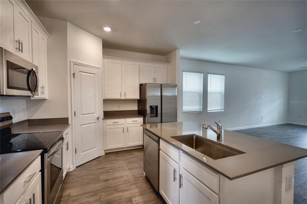 A kitchen features white cabinets, stainless steel appliances, a center island, and wood-look flooring — 6032 BLISSFUL STREET, CLERMONT, FL