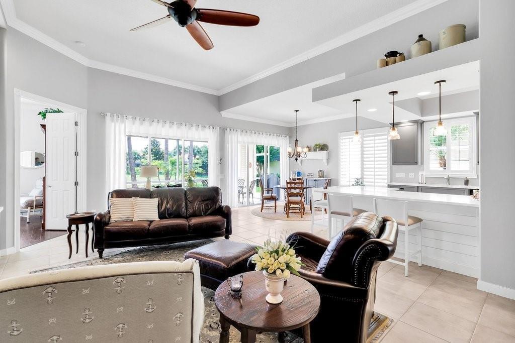 An open-concept living room and kitchen feature tile floors, leather furniture, and a ceiling fan — VERO BEACH, FL