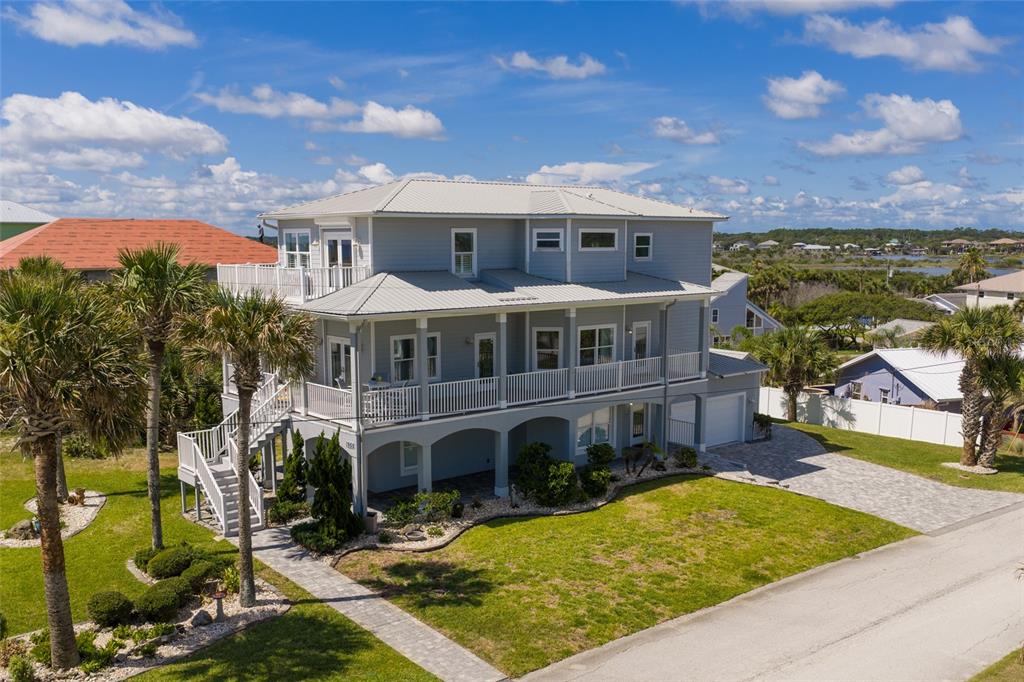 An elevated, three-story gray house with a metal roof and wraparound balconies sits on grass — 1955 N CENTRAL AVENUE, FLAGLER BEACH, FL