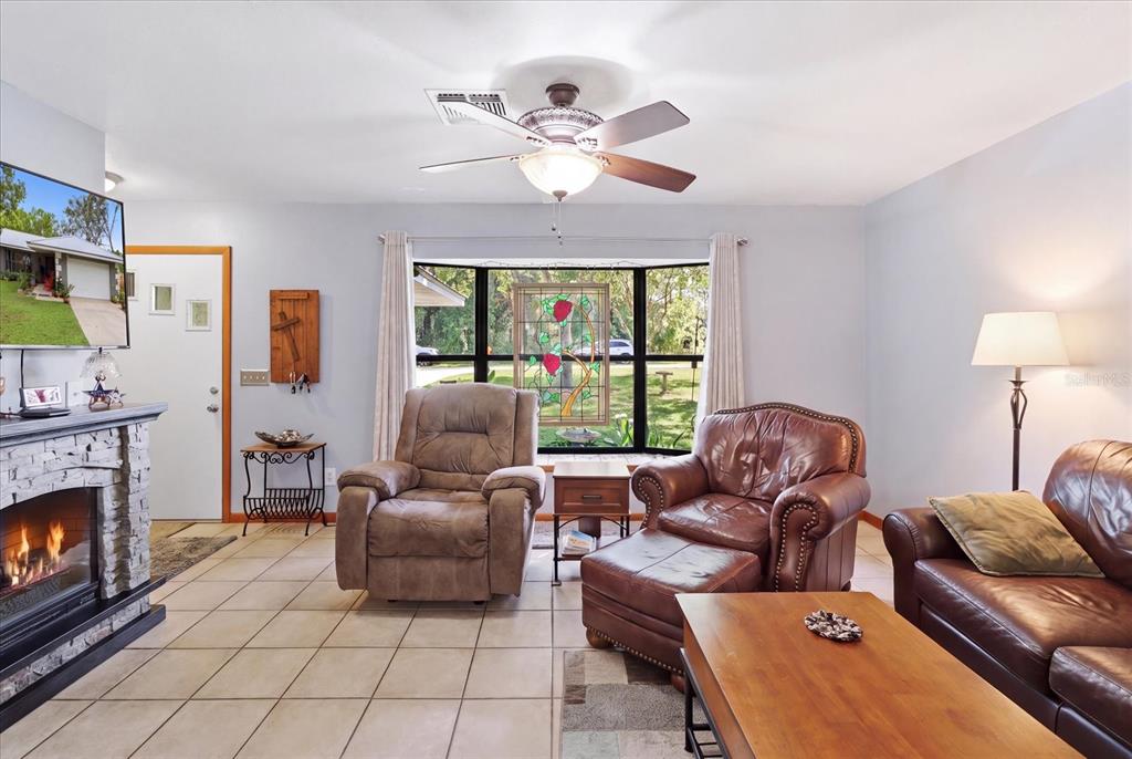 A living room features a stone fireplace, tile flooring, leather furniture, and a bay window — 9188 N COMMODORE DRIVE, CITRUS SPRINGS, FL