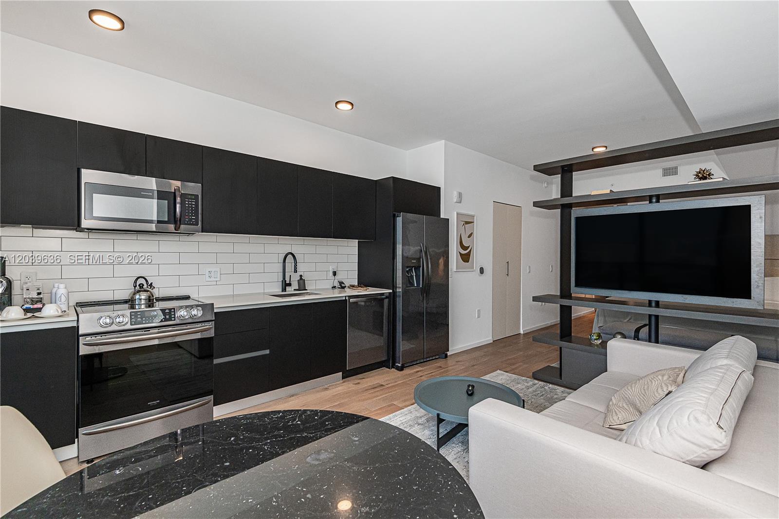 A modern kitchen with black cabinetry and stainless steel appliances opens into a living area — 398 NE 5th St # 2904, Miami FL 33132, MIAMI, FL