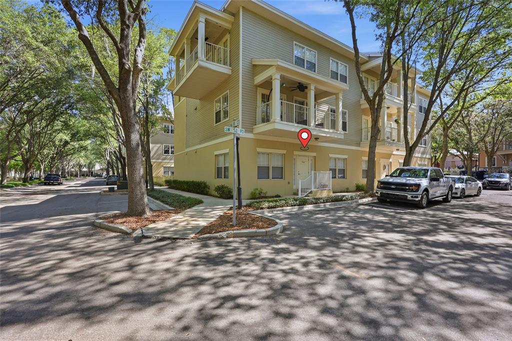 A three-story tan building with balconies and a street sign stands near a parking lot — 9172 SW 52ND ROAD UNIT 103, GAINESVILLE, FL