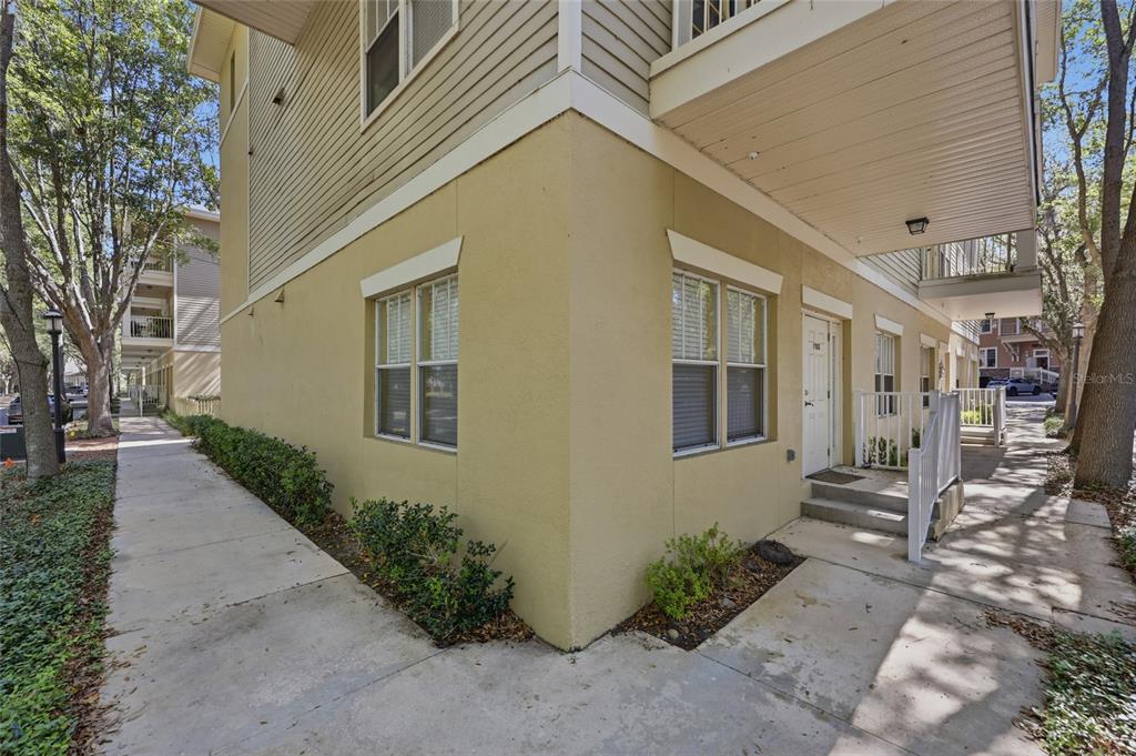 Exterior view of a multi-story apartment building with tan stucco walls and a concrete walkway — 9172 SW 52ND ROAD UNIT 103, GAINESVILLE, FL