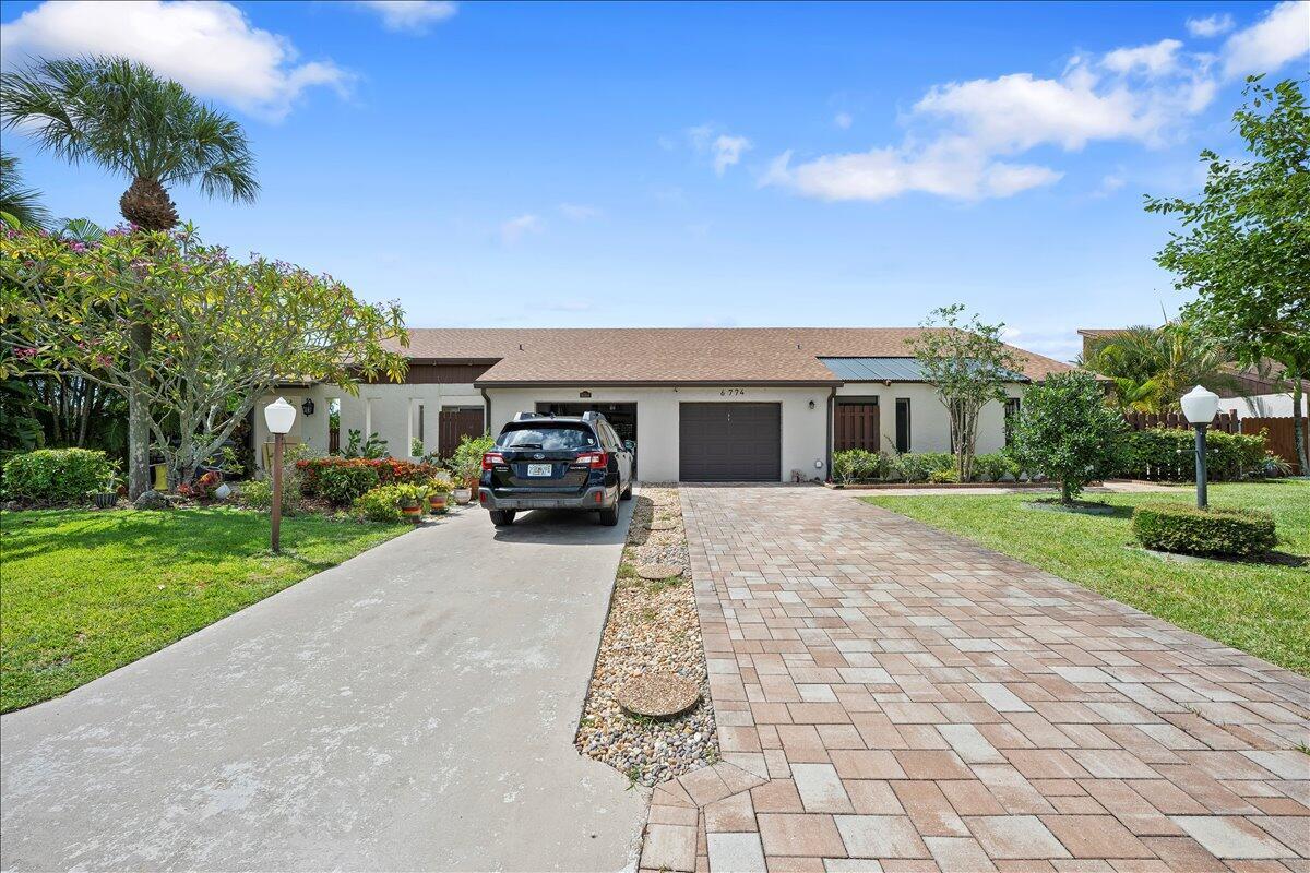 A single-story house features a paved driveway, a two-car garage, and a landscaped front yard — 6774 Wheaton Lane, Lake Worth FL 33467, LAKE WORTH, FL