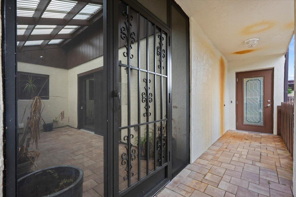 A covered patio with a security screen door, tiled flooring, and a brown entry door — 6774 Wheaton Lane, Lake Worth FL 33467, LAKE WORTH, FL