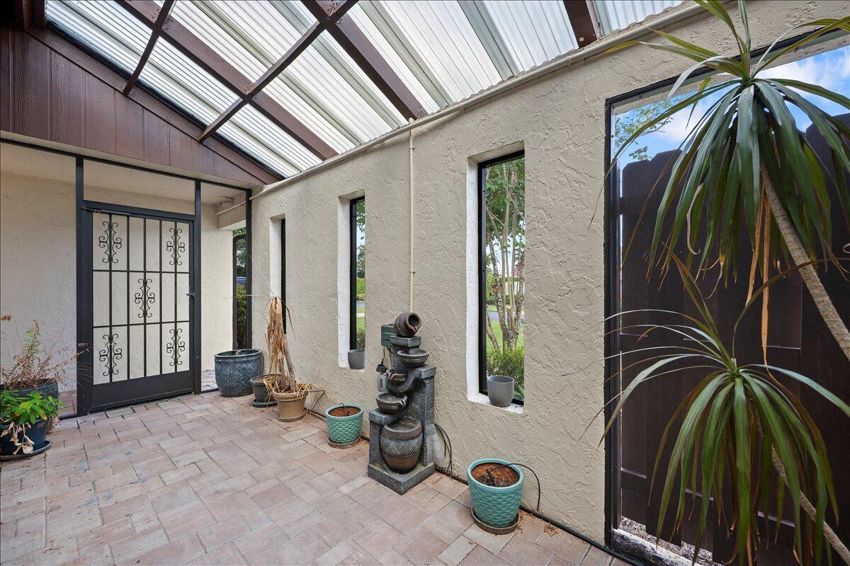 A covered patio features brick flooring, a decorative metal door, and a tiered water fountain — 6774 Wheaton Lane, Lake Worth FL 33467, LAKE WORTH, FL