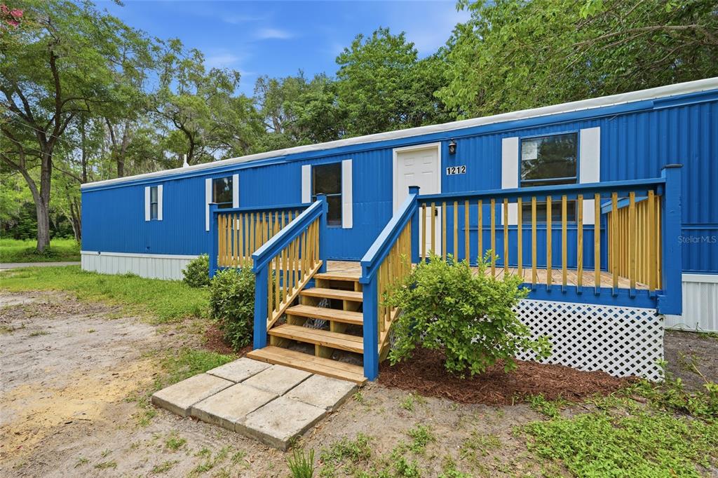 A blue mobile home with a wooden deck and stairs sits on a grassy lot — 1212 NE 1ST AVENUE, WILLISTON, FL