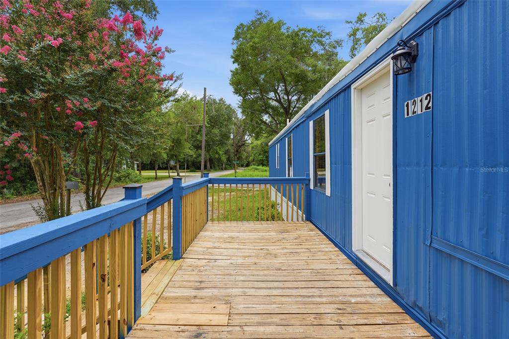 A wooden deck with blue railings leads to the white door of a blue home — 1212 NE 1ST AVENUE, WILLISTON, FL