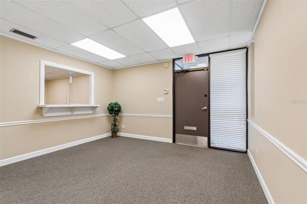 An office room features beige walls, gray carpeting, a service window, and an exit door — 1046 W BUSCH BOULEVARD UNIT 100, TAMPA, FL