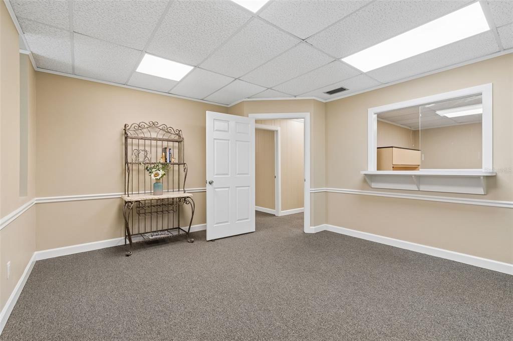 An interior room with beige walls, gray carpet, a metal baker's rack, and a service window — 1046 W BUSCH BOULEVARD UNIT 100, TAMPA, FL
