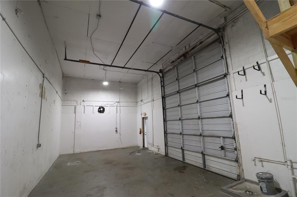 An industrial warehouse space features a concrete floor, white walls, and a large roll-up door — 1158  # 8 MARKET CIRCLE UNIT 8, PORT CHARLOTTE, FL