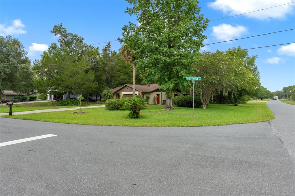 A single-story house sits on a corner lot with a large lawn and mature trees — 4856 S DRIFTWOOD WAY, HOMOSASSA, FL