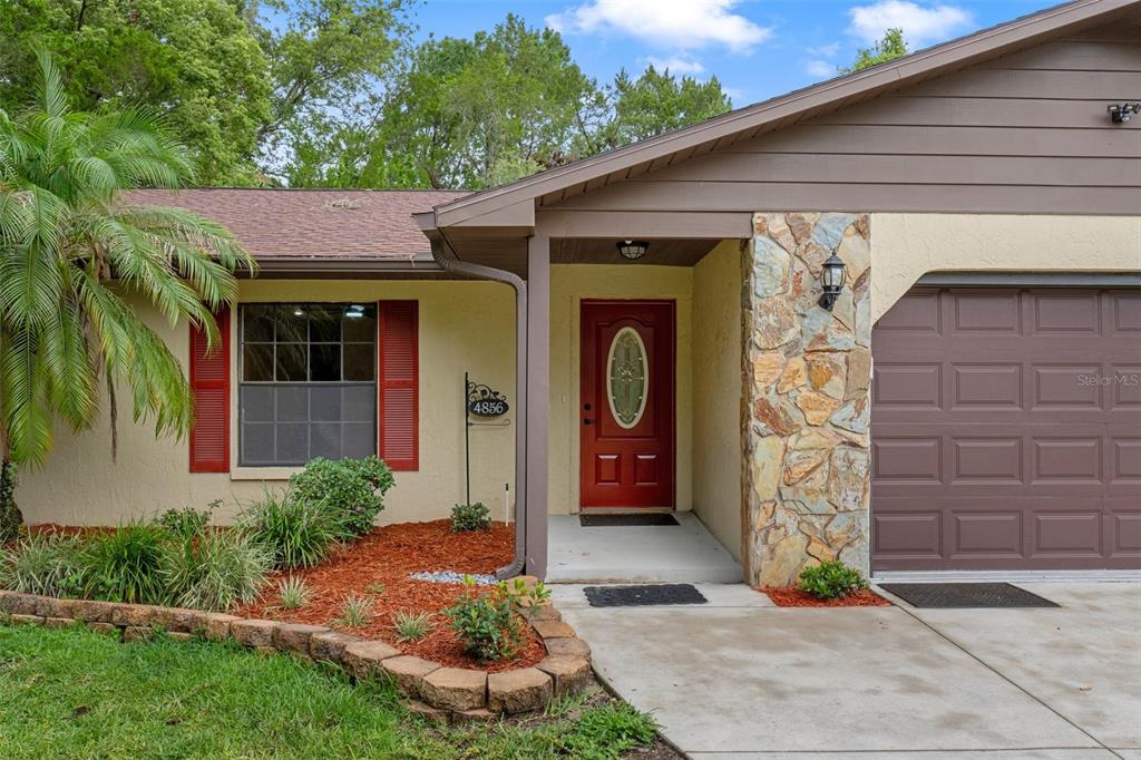 A single-story house exterior features a red front door, stone siding, and a brown garage — 4856 S DRIFTWOOD WAY, HOMOSASSA, FL